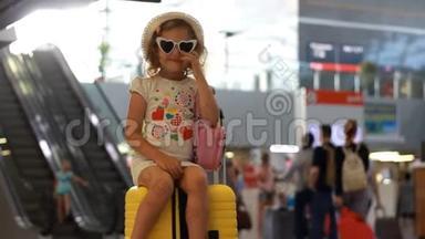 儿童游客坐在火车站的一个黄色的大皮箱上。 小女孩正在等待出发，在